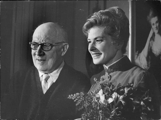 G. Molander et Ingrid Bergman en 1964, dans un cadre intérieur formel, la femme tenant un bouquet de fleurs.
