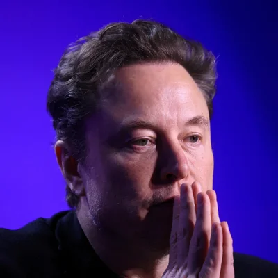 Portrait d'Elon Musk, les mains jointes, sur fond bleu.