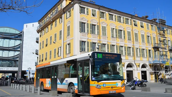 Bus de la ligne 208 du réseau Lignes d'Azur circulant dans une rue de Nice, devant un bâtiment jaune et une structure moderne.