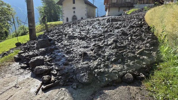 Une spectaculaire coulée de boue recouvre la route d'un hameau, avec une chapelle en arrière-plan.