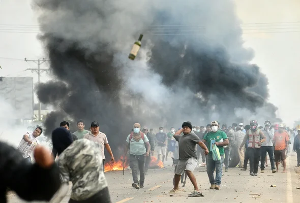 Manifestants sur une route barricadée, avec des incendies et un jet de bouteille lors d'affrontements.