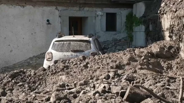 Une voiture blanche ensevelie sous la boue devant un bâtiment touché par la coulée torrentielle.