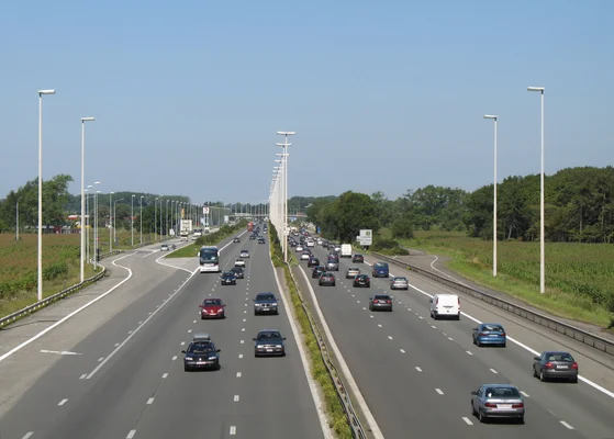Vue de l'autoroute E40 à Jabbeke, en Belgique, sous un ciel clair, avec une circulation fluide et des champs verdoyants.