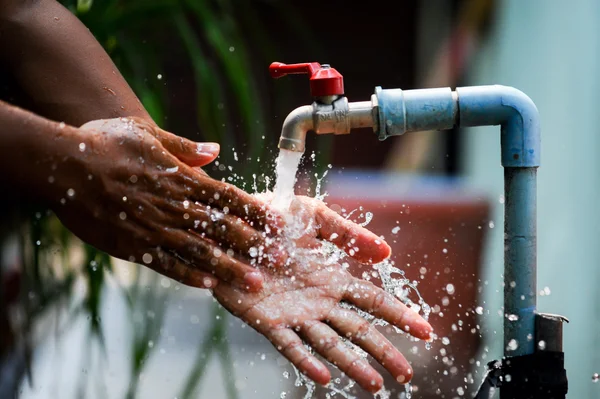 Une personne recueille de l'eau à un robinet extérieur, évoquant les mesures de rationnement face à la sécheresse.