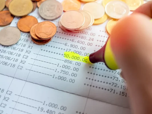 Main surlignant un chiffre sur un document financier, entouré de pièces de monnaie.