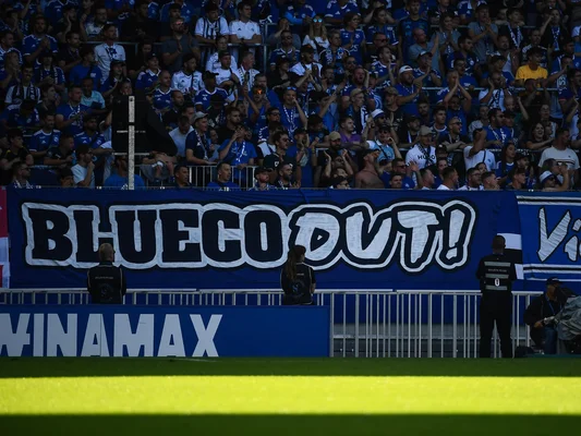 Supporters brandissant une banderole 'BLUECO OUT!' dans un stade.