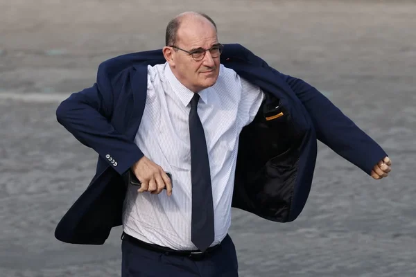 Jean Castex ajustant sa veste de costume à l'extérieur, téléphone en main.
