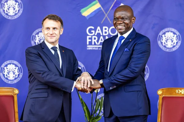 Rencontre diplomatique entre le Gabon et la France, symbolisée par une poignée de main devant les drapeaux des deux pays.