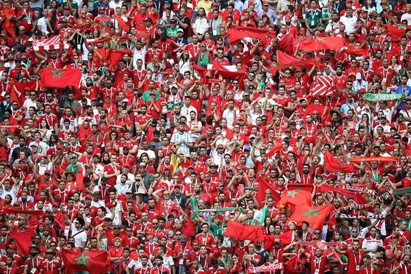 Supporters marocains en liesse dans un stade, vêtus de rouge et agitant des drapeaux du Maroc.