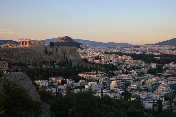 Vue panoramique d'Athènes au coucher du soleil, avec le Parthénon illuminé sur l'Acropole et la ville en arrière-plan.