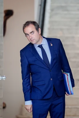 Sébastien Lecornu marchant avec des dossiers dans un bâtiment aux murs de pierre.