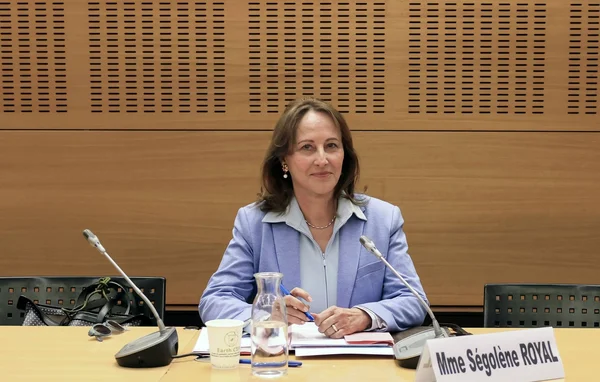 Ségolène Royal assise à une table de conférence avec micros et un écriteau à son nom.