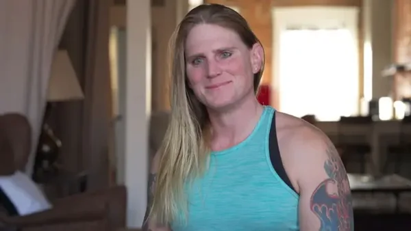 Portrait d'une femme aux cheveux blonds et tatouages dans un intérieur.