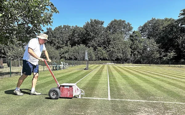 Christophe traçant les lignes de son court de tennis sur gazon avec une machine à marquer.