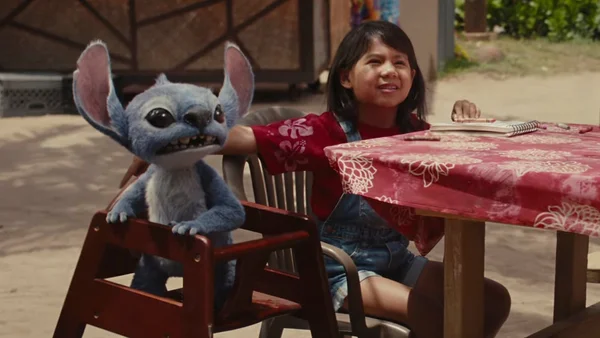 Scène du film Lilo & Stitch (2025) : Stitch assis à une table avec Lilo en extérieur.