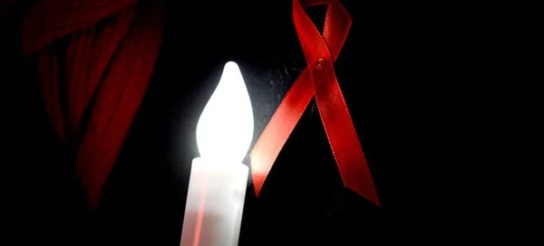 Symbole de la lutte contre le sida : ruban rouge et bougie allumée.