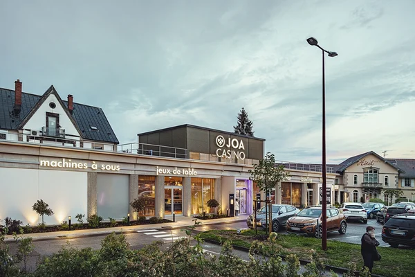 Vue extérieure du casino JOA au crépuscule, avec ses enseignes lumineuses et son parking.
