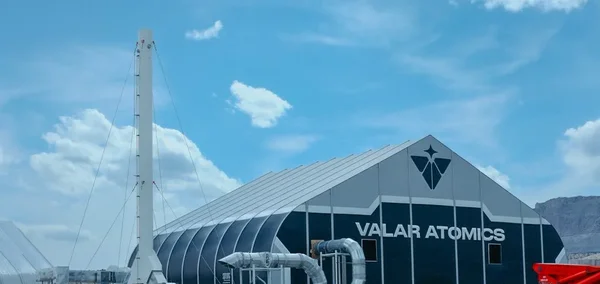 Installation industrielle de Valar Atomics avec une tour blanche et l'enseigne de l'entreprise sous un ciel bleu.