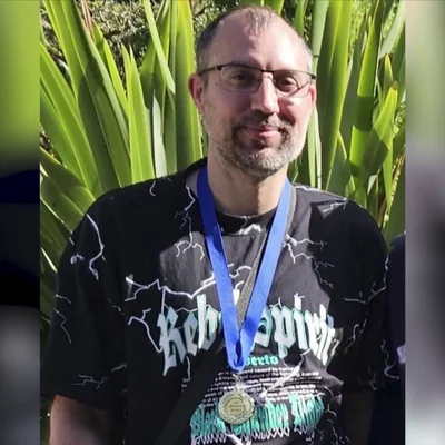 Jérôme Barella, souriant à l'extérieur devant des plantes vertes, portant un t-shirt noir et une médaille.