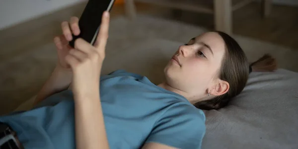 Une adolescente utilise son smartphone allongée sur son lit.