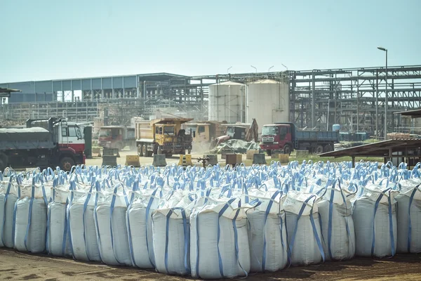 Site industriel de traitement de minerais, avec des sacs de matière première et des engins de chantier.
