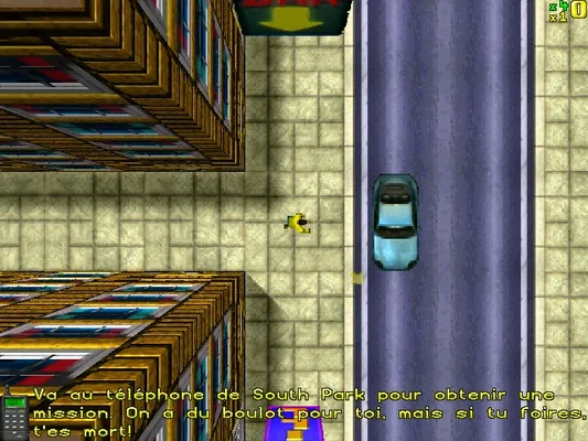 Capture d'écran in-game du jeu Grand Theft Auto (1997) montrant une vue de dessus en 2D. On y voit un personnage jaune sur le trottoir, une voiture bleue sur la route, et des bâtiments aux toits colorés. Un texte de mission en français est affiché en bas de l'écran : 'Va au téléphone de South Park pour obtenir une mission...'. L'interface utilisateur avec le score et les vies est visible en haut à droite.