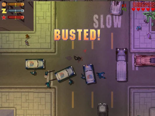 A top-down screenshot from Grand Theft Auto 2 (1999) showing a chaotic street scene with police cars, officers, and the player character being apprehended. The large text 'BUSTED!' is displayed prominently in the center, indicating a game-over state after being caught by law enforcement. UI elements like health, armor, money ($9852402), and weapon icons are visible.