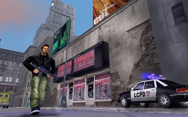 Capture d'écran du jeu vidéo Grand Theft Auto III (2001). L'image montre le protagoniste, Claude, armé d'un fusil d'assaut, courant dans les rues de Liberty City. En arrière-plan, on aperçoit un magasin 'Porno Video', une voiture de police marquée 'LCPD' avec ses gyrophares allumés, et des immeubles urbains.