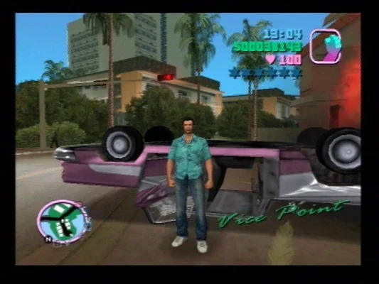 Capture d'écran du jeu vidéo Grand Theft Auto: Vice City (2002), montrant le personnage principal, Tommy Vercetti, debout devant une voiture renversée dans un décor urbain tropical. L'interface utilisateur du jeu est visible, incluant la carte, l'argent, la santé et les étoiles de recherche.