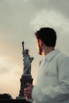 Un homme en veste blanche contemple la statue de la Liberté au loin.
