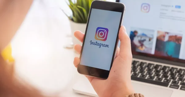 Smartphone affichant le logo Instagram avec un ordinateur portable en arrière-plan.