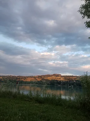 Vue du lac de Paladru depuis le village de Paladru au coucher du soleil, une lumière dorée et un ciel chargé de mystère.