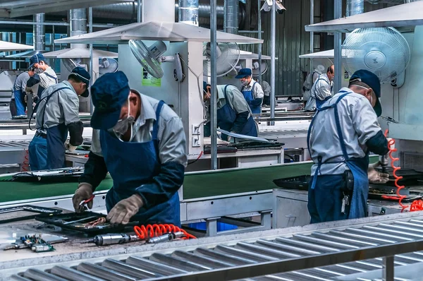 Ouvriers sur une chaîne d'assemblage dans une usine, illustrant les conditions de travail des ouvriers.