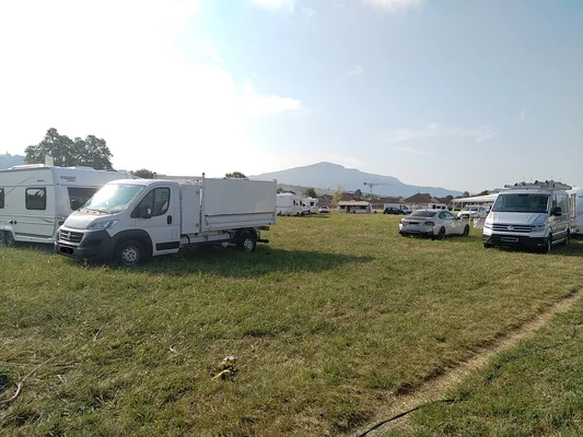 Campement de camping-cars et véhicules utilitaires sur un champ, avec des montagnes en arrière-plan.