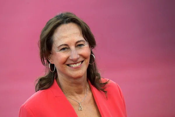 Ségolène Royal, souriante, en blazer corail devant un fond rose.