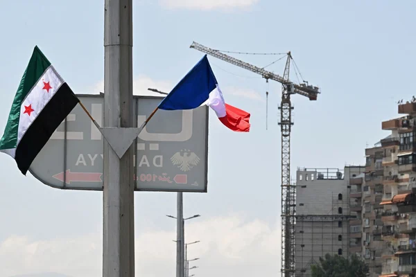 Les drapeaux de l'opposition syrienne et de la France hissés dans un environnement urbain.