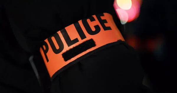 Brassard de police orange, symbole de l'enquête en cours.