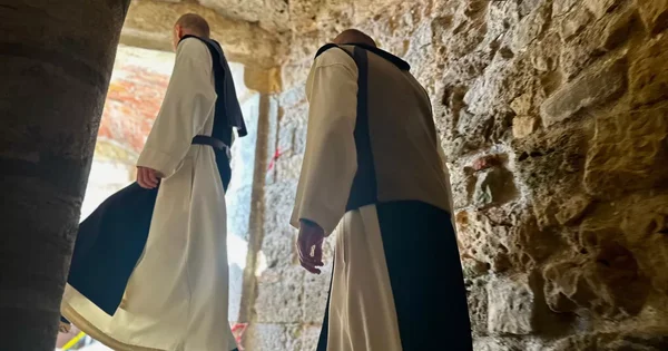 Deux moines bénédictins marchant dans un couloir de pierre de l'abbaye.