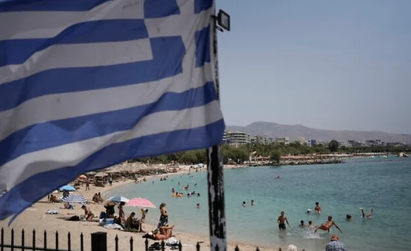Drapeau grec sur une plage fréquentée, symbole du retour des expatriés.
