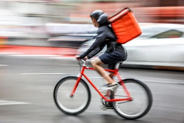 Livreur à vélo transportant une commande dans un sac thermique, illustrant les conditions de travail exposées à la chaleur.