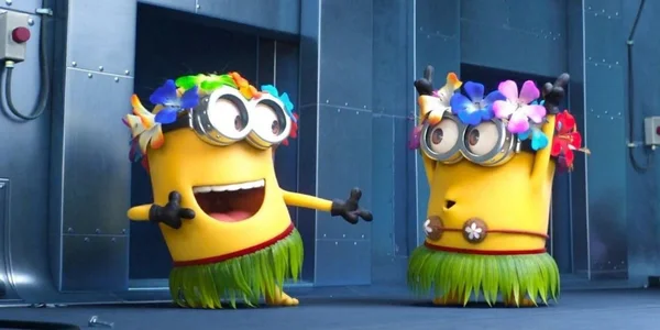 Deux Minions vêtus de tenues hawaïennes, arborant jupes en herbe et colliers de fleurs, devant un mur industriel métallique.