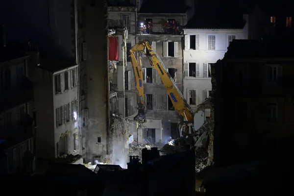 Une pelleteuse jaune démolit un immeuble effondré à Marseille, sous les yeux des secouristes postés sur les balcons voisins.