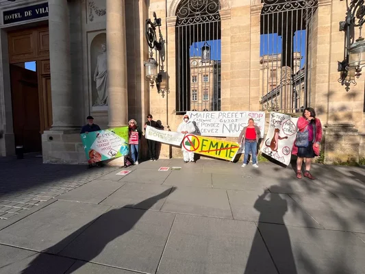 Opposants au projet EMME devant l'hôtel de ville, avec une personne en combinaison de protection blanche.