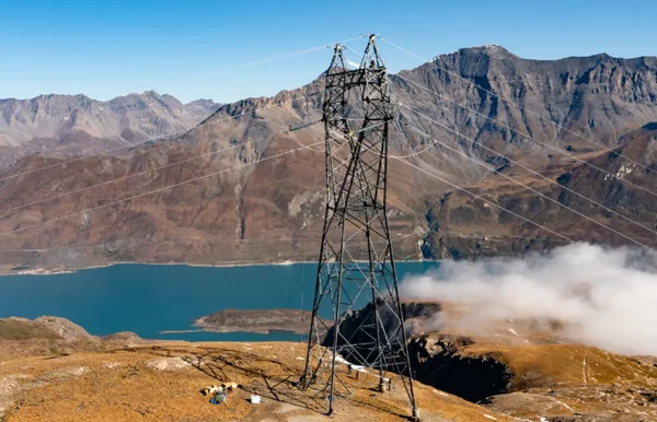 Pylône haute tension du réseau RTE sur une crête montagneuse surplombant un lac de retenue turquoise.