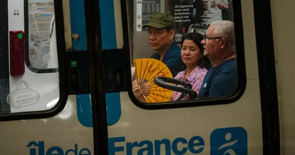 Voyageurs dans un métro francilien, l'un d'eux utilisant un éventail pour se rafraîchir.