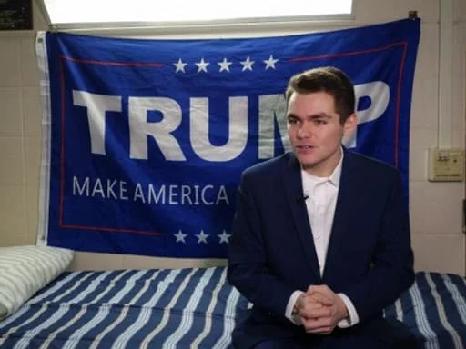 Nick Fuentes posant devant un drapeau Trump dans une chambre.