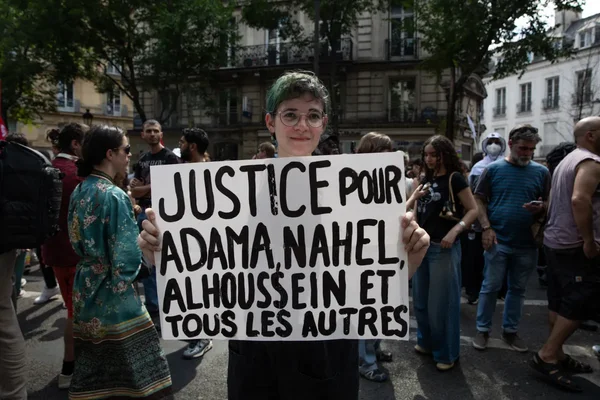 Participant à une marche avec une pancarte 'Justice pour Adama, Nahel, Alhoussein et tous les autres'.