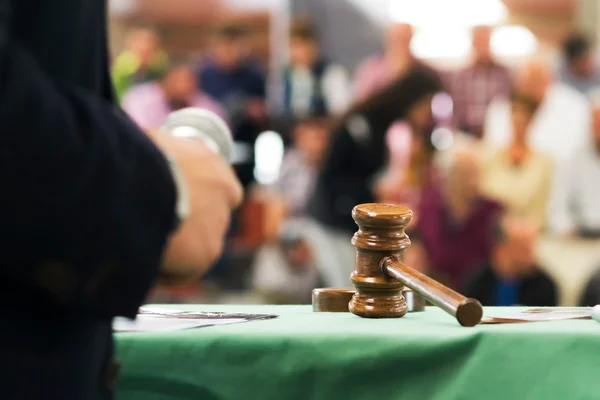 Marteau de commissaire-priseur sur une table verte lors d'une vente aux enchères judiciaires, avec l'audience visible en arrière-plan.
