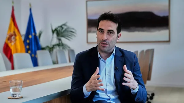 Le ministre de l'Économie s'exprimant lors d'une interview avec les drapeaux espagnol et européen.