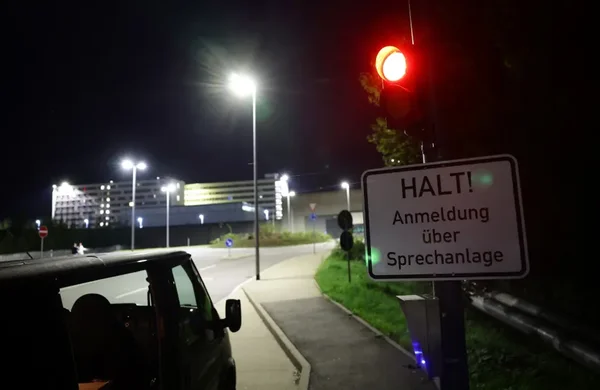 Véhicule arrêté à un feu rouge près d'un panneau d'arrêt en Allemagne, avec un bâtiment illuminé en arrière-plan.